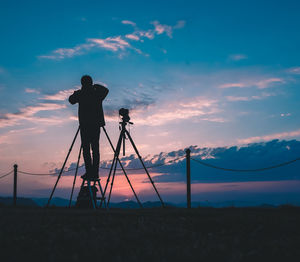 Silhouette man photographing on field against sky during sunset