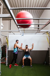 Young athletic male in sportswear performing squats while training in modern gym with instructor