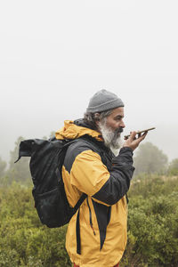 A man picks up the signal on his mobile phone and sends a voice message, hiker with backpack 