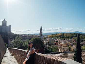 Side view of woman sitting against buildings in city