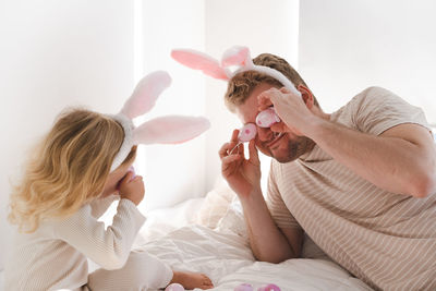 Father and daughter at home celebrating easter wearing rabbit ears playing with eggs