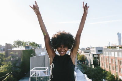 Happy young woman standing on rooftop in brookly making victory sign