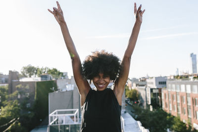 Happy young woman standing on rooftop in brookly making victory sign