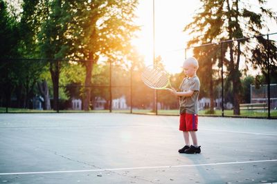 Boy holding tennis racket while standing at court