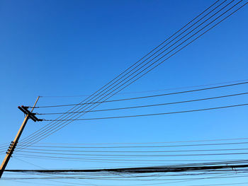 Low angle view of electricity pylon against clear blue sky