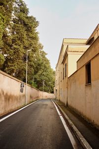 Empty road along buildings and trees against sky