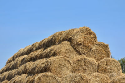 Low angle view of hay bales on field against clear blue sky