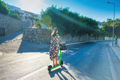 Young beautiful woman in dress rides an electric scooter on empty asphalt road. electric urban 
