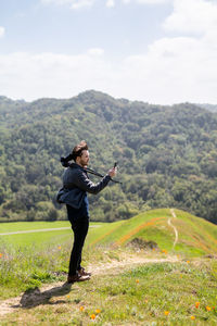 Young man takes photo with phone while holding camera over shoulder