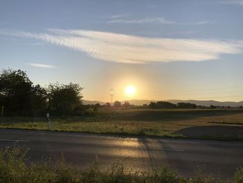 Road amidst field against sky during sunset