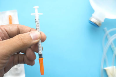 Close-up of hand holding syringe over blue table
