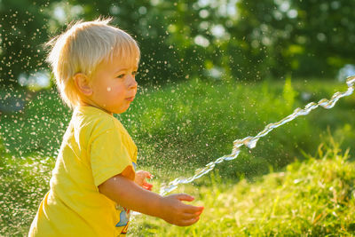 Cute little boy watering flowers in the garden. young child splashing water from garden water hose.