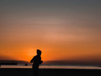 Silhouette woman standing on beach against sky during sunset