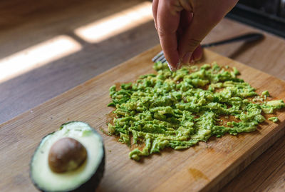 Close-up of person preparing mashed avocado on wooden cutting board