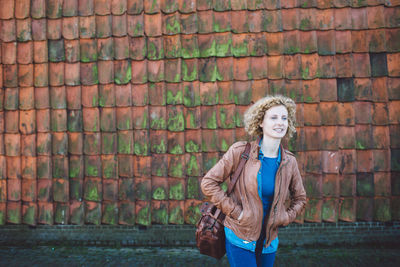 Portrait of young woman standing against brick wall