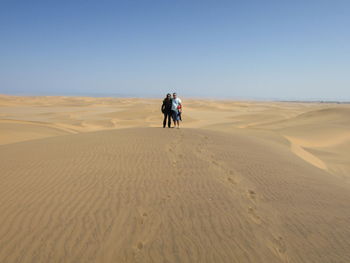 Man and woman standing at desert against clear sky