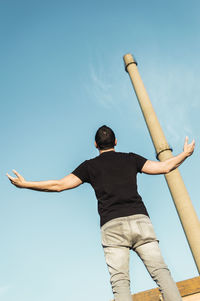 Rear view of man with arms outstretched against blue sky