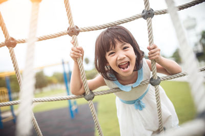 Portrait of girl screaming while leaning on jungle gym in playground