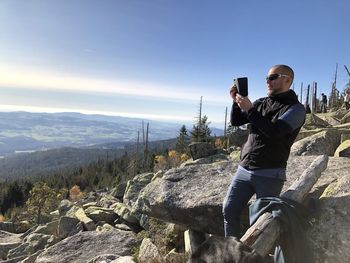 Man photographing on mobile phone against sky