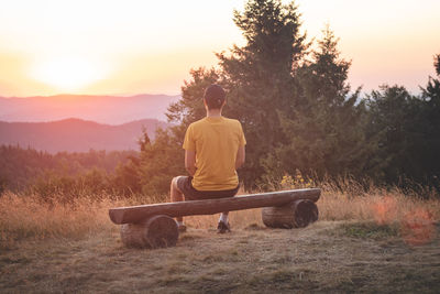 Enthusiastic traveler sits on a wooden bench and watches the last remnants of sunshine in the raw