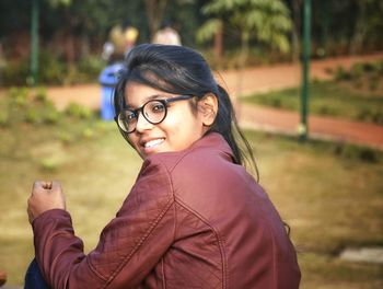 Side view portrait of smiling girl wearing jacket sitting in public park