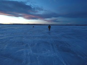 Person walking on snow covered land against sky during winter