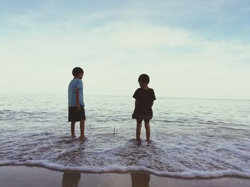 Rear view of father and daughter standing on beach against sky