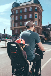 Rear view of father cycling while daughter sitting on back seat in city