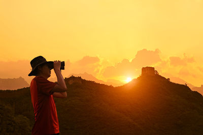 Side view of man looking through binoculars against great wall of china during sunset