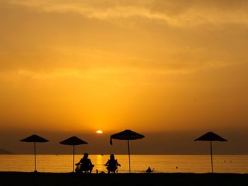 Silhouette people on beach against orange sky