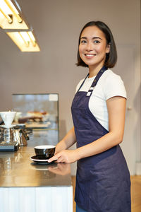 Portrait of smiling young woman holding coffee at home