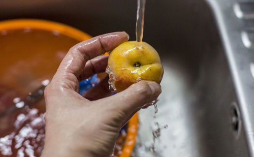 Cropped image of person hand holding apple over running water in sink