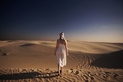 Woman walking on sand dune against sky