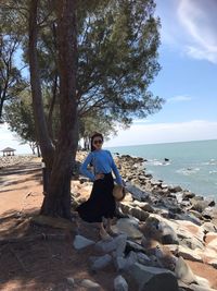 Woman standing on rock by sea against tree