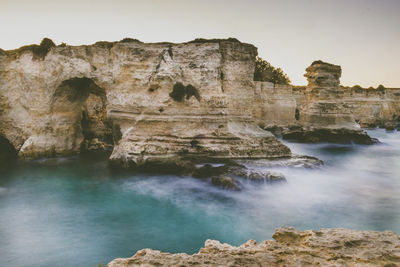 Rocky cliff by sea against sky