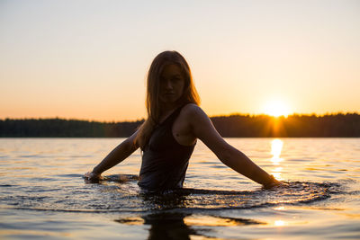 Girl in a long black swimsuit swims outside the city on the lake in the rays of sunset or dawn.