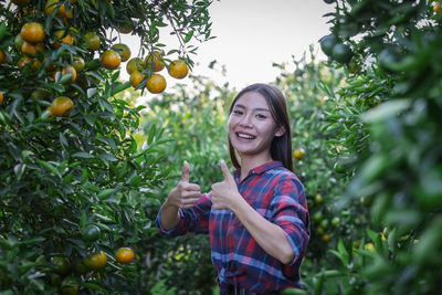 Smiling young woman standing against trees and plants