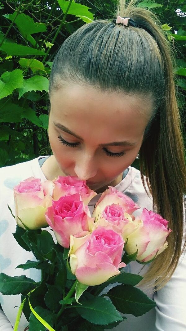 flower, rose - flower, petal, fragility, nature, beauty in nature, freshness, outdoors, bouquet, flower head, smelling, one person, day, pink color, beautiful woman, eyes closed, plant, leaf, close-up, real people, beauty, florist, young adult, people