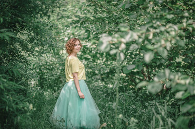 Portrait of young woman standing by plants