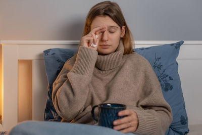 Sick woman holding coffee cup resting on bed