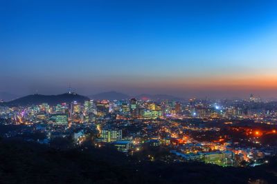 Aerial view of illuminated cityscape against blue sky at night