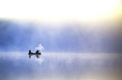 Silhouette people on boat in lake during foggy weather