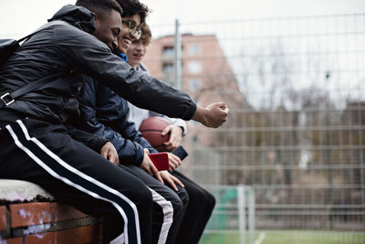 Happy male friends taking selfie while sitting on retaining wall after basketball practice in winter