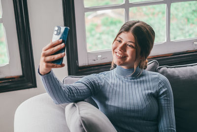 Young woman using mobile phone while sitting on sofa at home