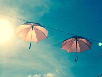 Low angle view of umbrellas hanging on rope against blue sky during sunny day