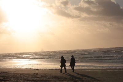 Silhouette female friends walking at beach during sunset