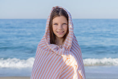 Portrait of a young girl wrapped in a towel against the blue sky and the sea.