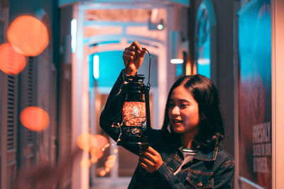 Young woman holding oil lantern at aisle during night