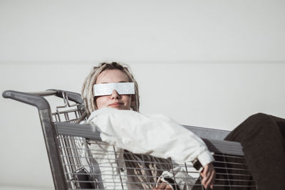 Young woman with dreadlocks sitting in shopping cart against wall