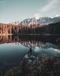 Rear view of woman standing at lakeshore against mountains